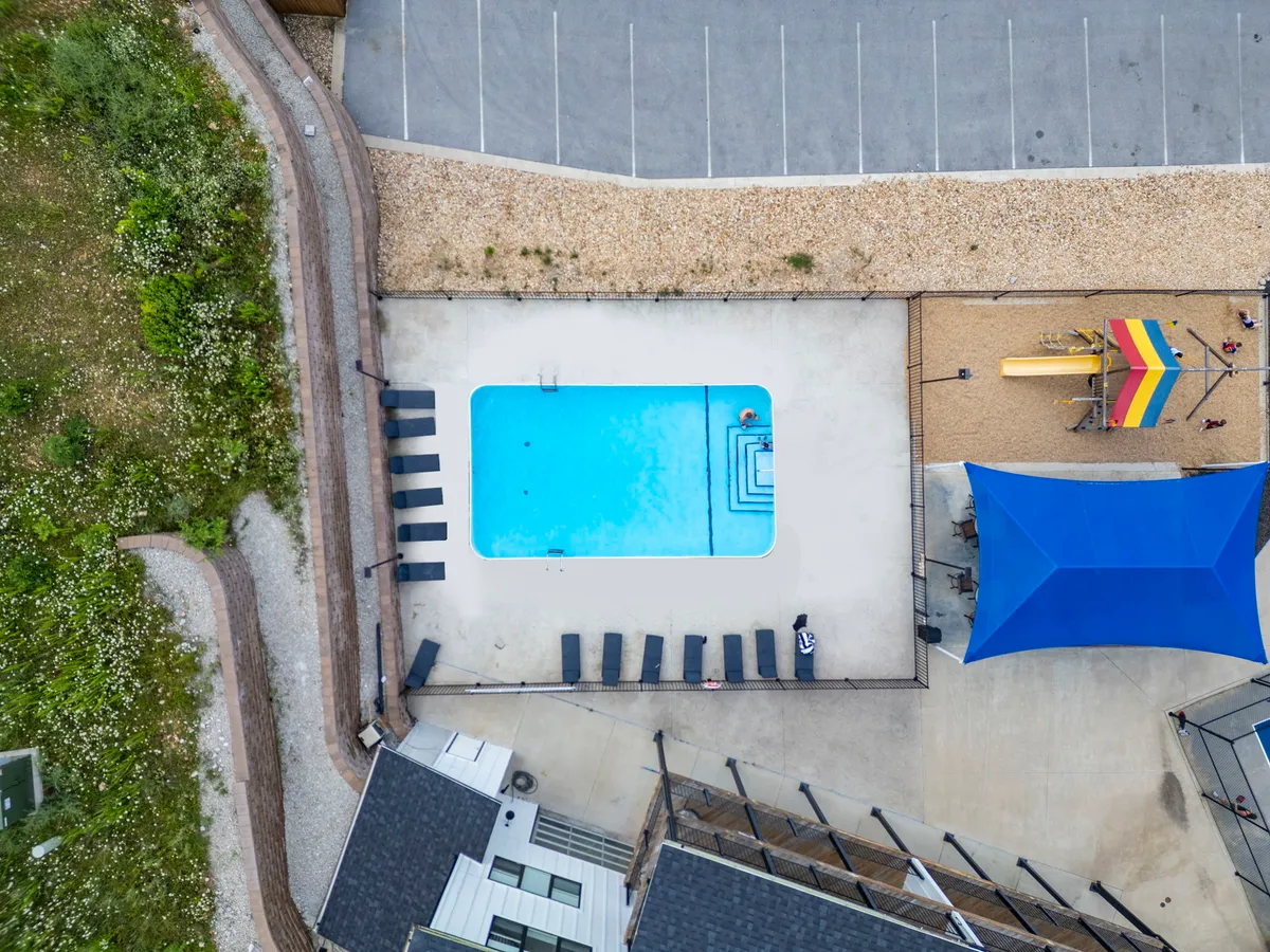 This exterior image shows a resort-style swimming pool surrounded by lounge chairs, with a colorful playground area visible in the background. Shade structures provide comfort for families, and the scene is set on a sunny day, inviting both children and adults to relax or play.