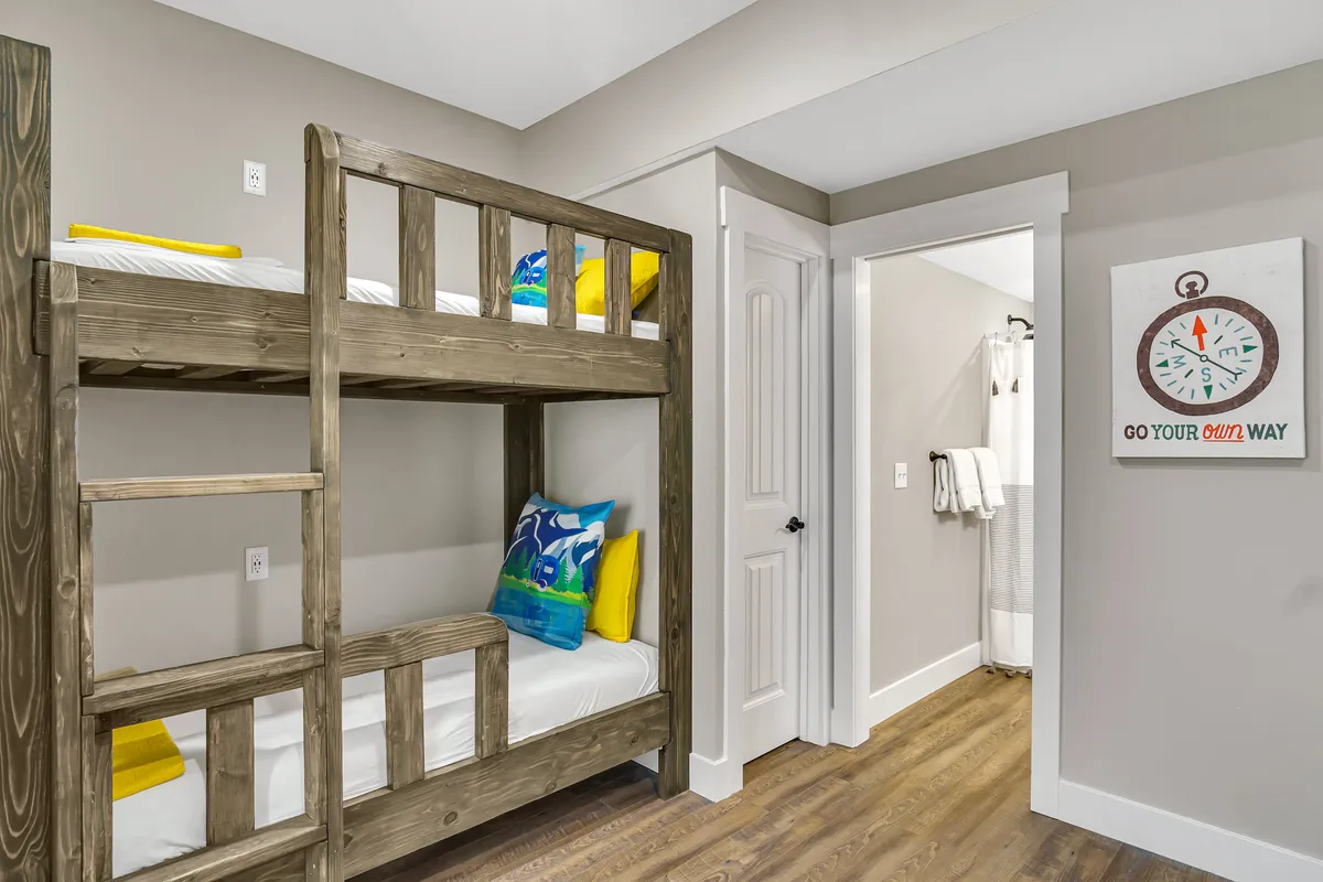 A cheerful bunk room setup with twin bunk beds adorned with colorful pillows and decorative wall art. The space is designed for both play and rest, offering a cozy and inviting environment for children or groups.