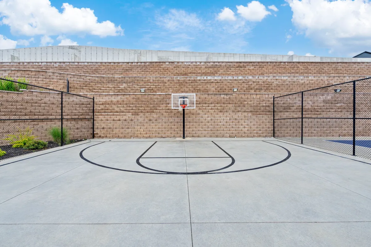 An outdoor basketball court with clear court markings and a surrounding fence, inviting guests for friendly matches or practice. The space is open and energetic, ideal for group sports and community events.