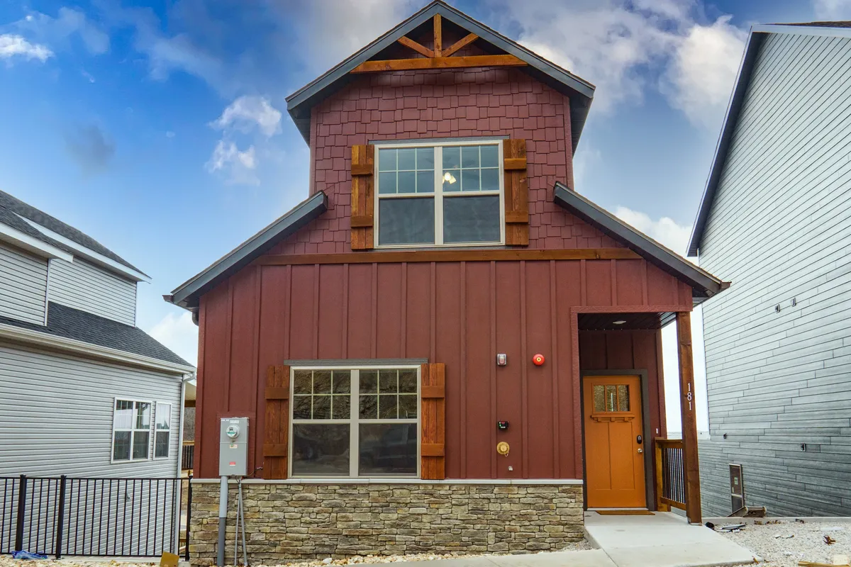 This exterior view highlights the home's inviting front door, large windows, and a sturdy stone base accented with wood. The welcoming facade signals both privacy and the standalone nature of the property, while large windows hint at bright, modern interiors.