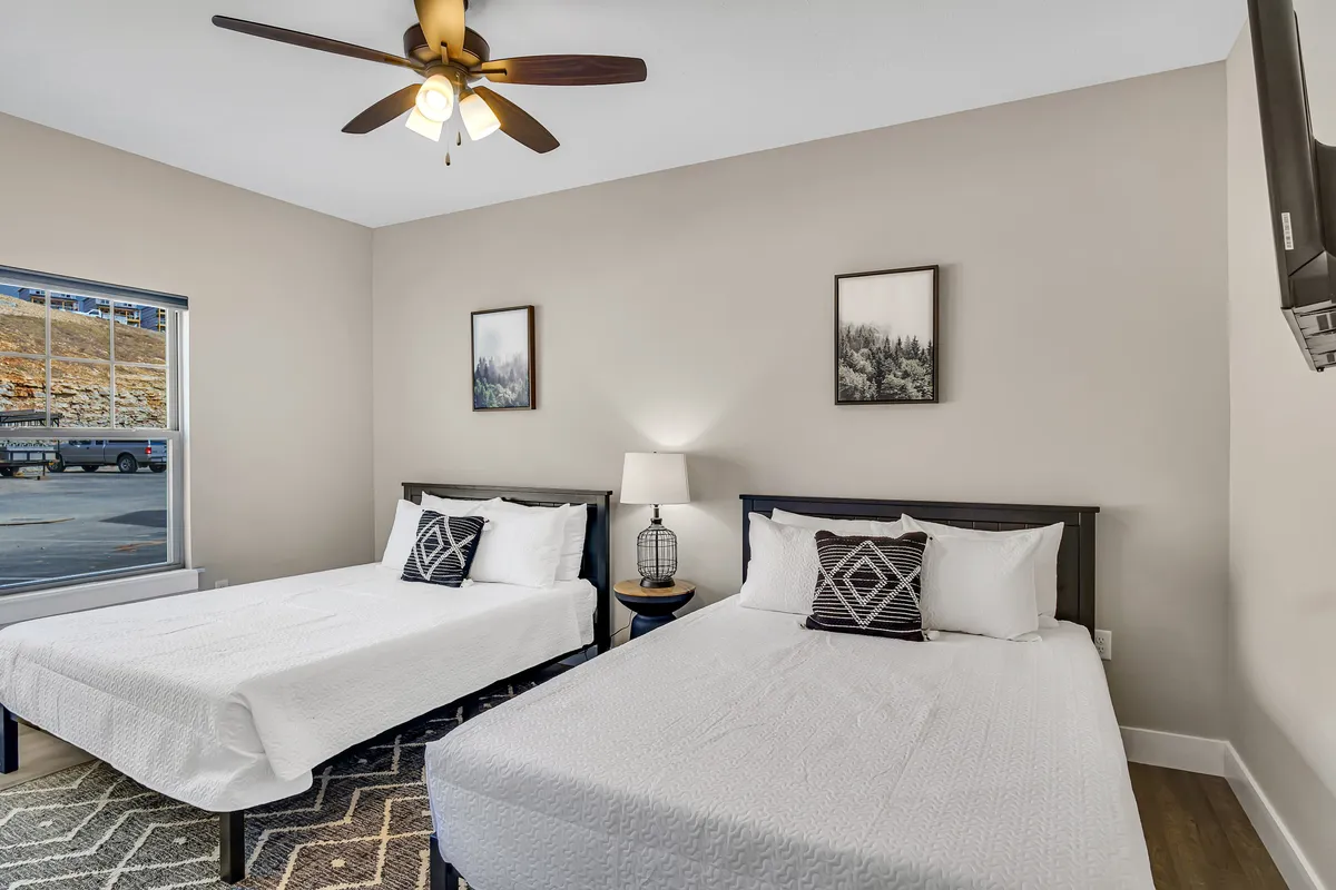 A tranquil bedroom featuring two beds with soft linens, a window offering natural light, decorative art frames, and a bedside lamp. The color scheme is soothing, creating a serene retreat for unwinding.