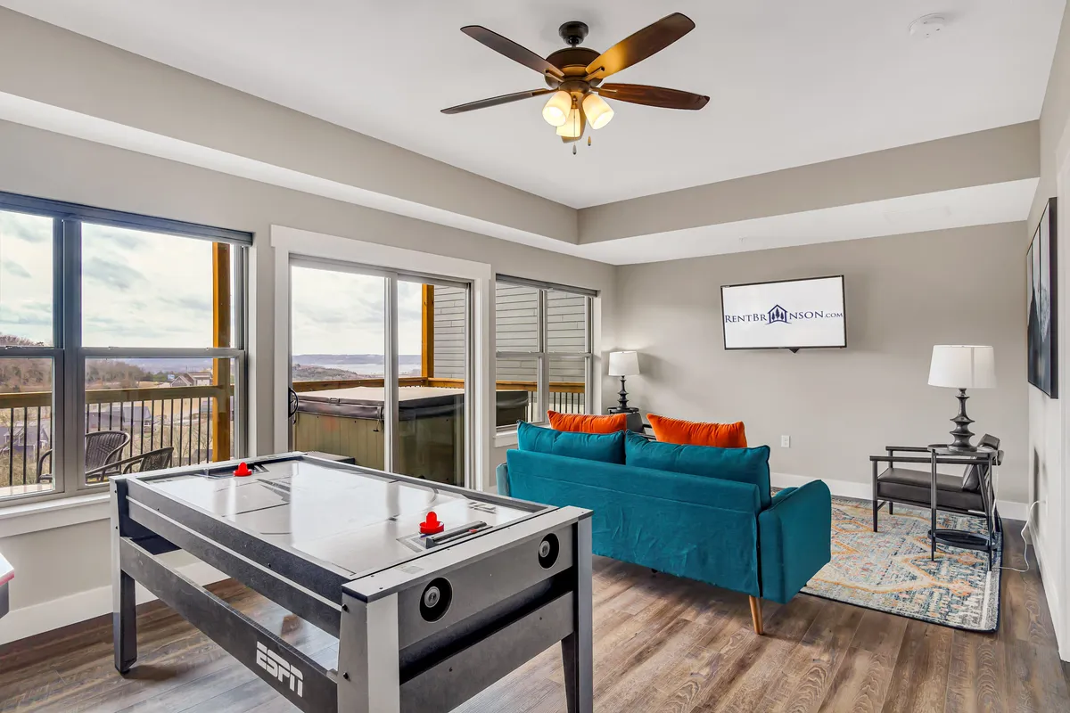An inviting interior space featuring a comfortable sofa and a prominent air hockey table, positioned in front of large windows that let in natural light. The space feels playful yet cozy, suitable for family gaming and relaxation after a day outdoors.