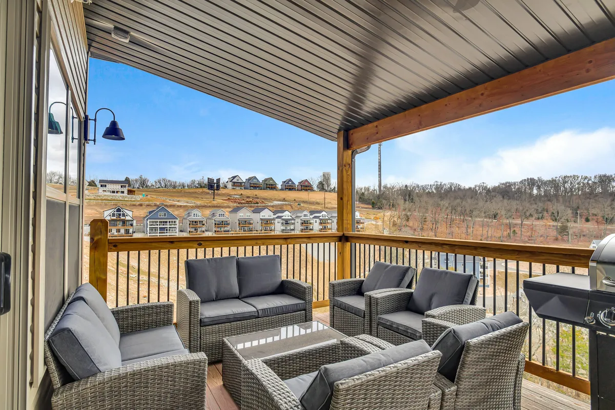 An elevated deck with a comfortable seating area, a sleek outdoor grill, and sweeping panoramic views of the surrounding hills. The scene is set for outdoor dining or relaxing with friends as the sun sets beyond the horizon.