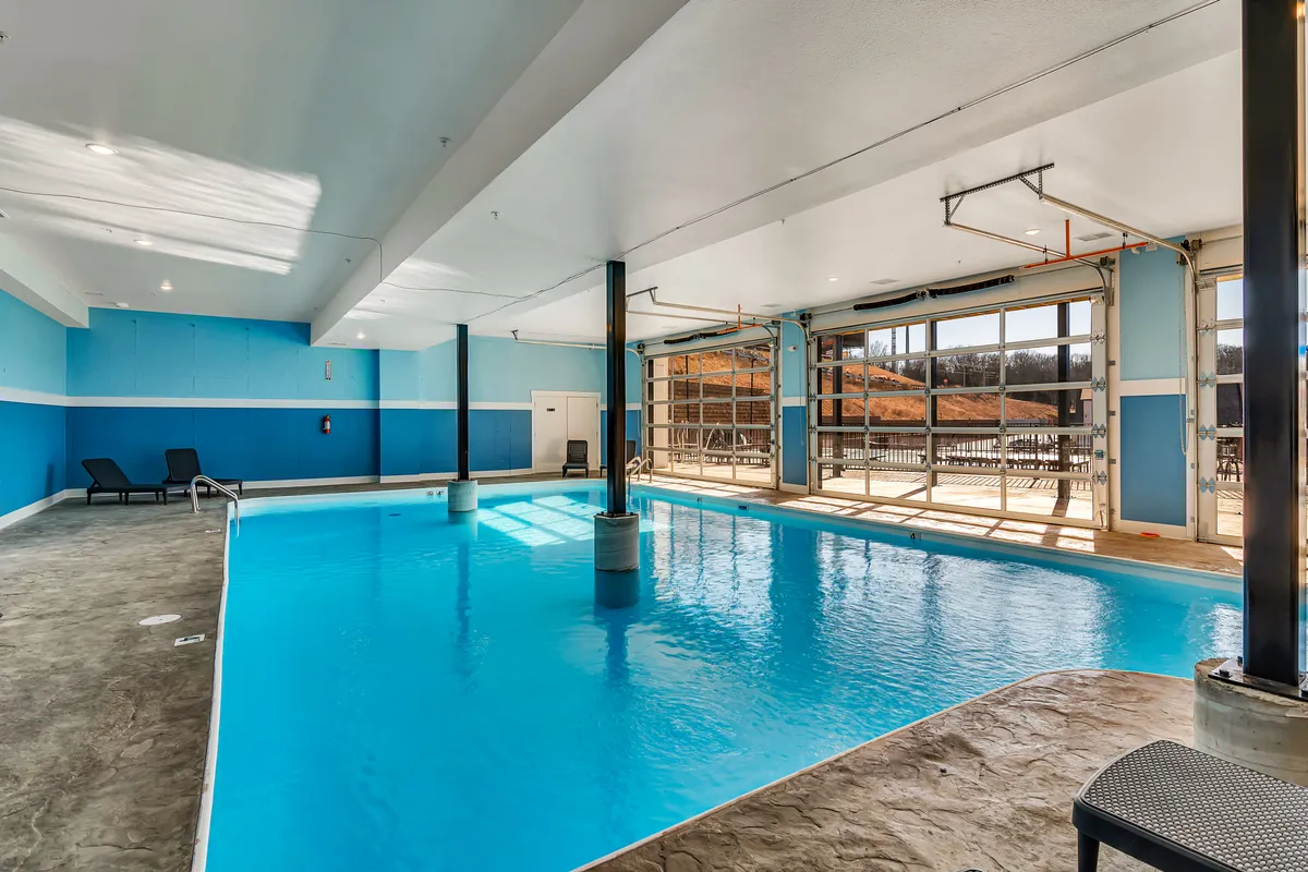 A serene interior space featuring a spacious indoor swimming pool, large windows that let in natural light, and poolside chairs for relaxation. The tranquil atmosphere invites year-round swimming and leisurely poolside moments.